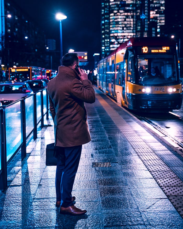 services-03 A professional man in a coat makes a phone call at a tram stop in Warsaw at night.