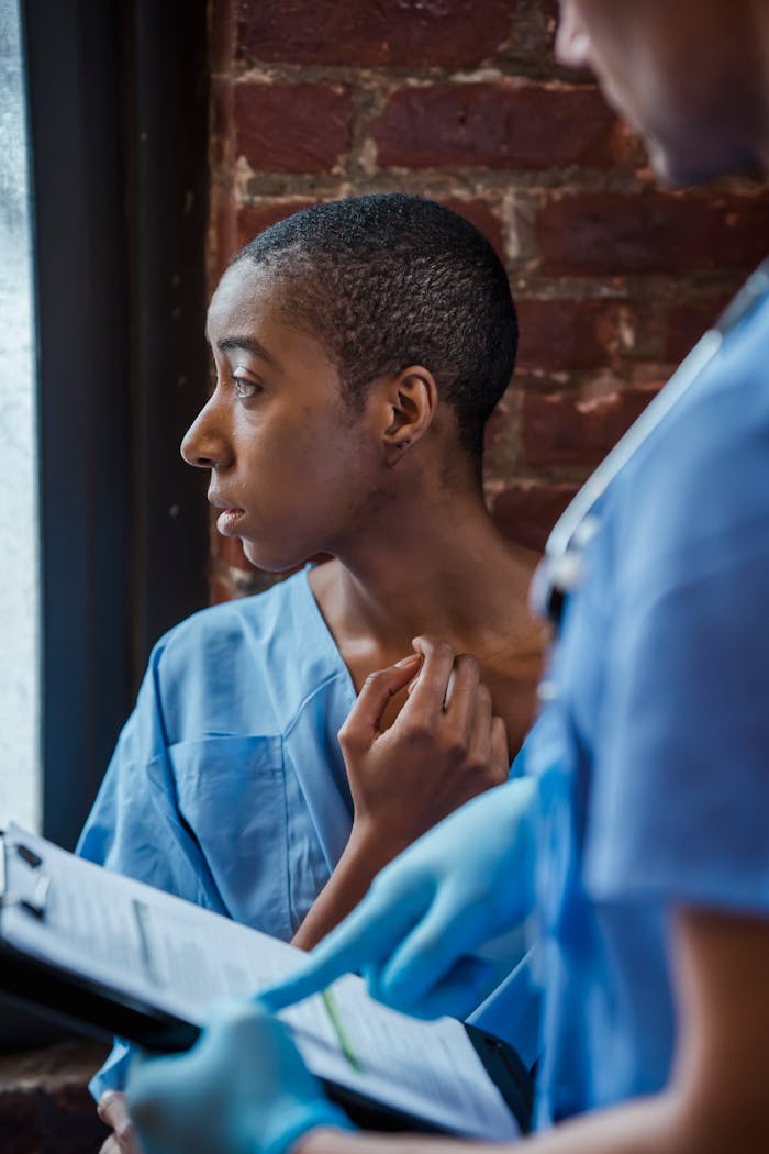 services-01 Crop unrecognizable nurse in medical uniform standing with clipboard with diagnosis near thoughtful African American patient in hallway of hospital in daytime